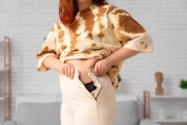 Image of woman trying to do her trousers up after pregnancy weight gain Banstead