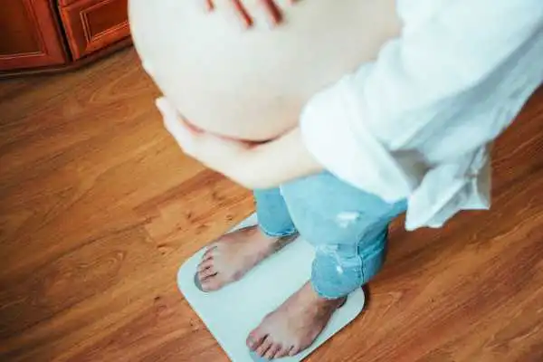 Image of woman weighing herself and experiencing weight gain through pregnancy Banstead